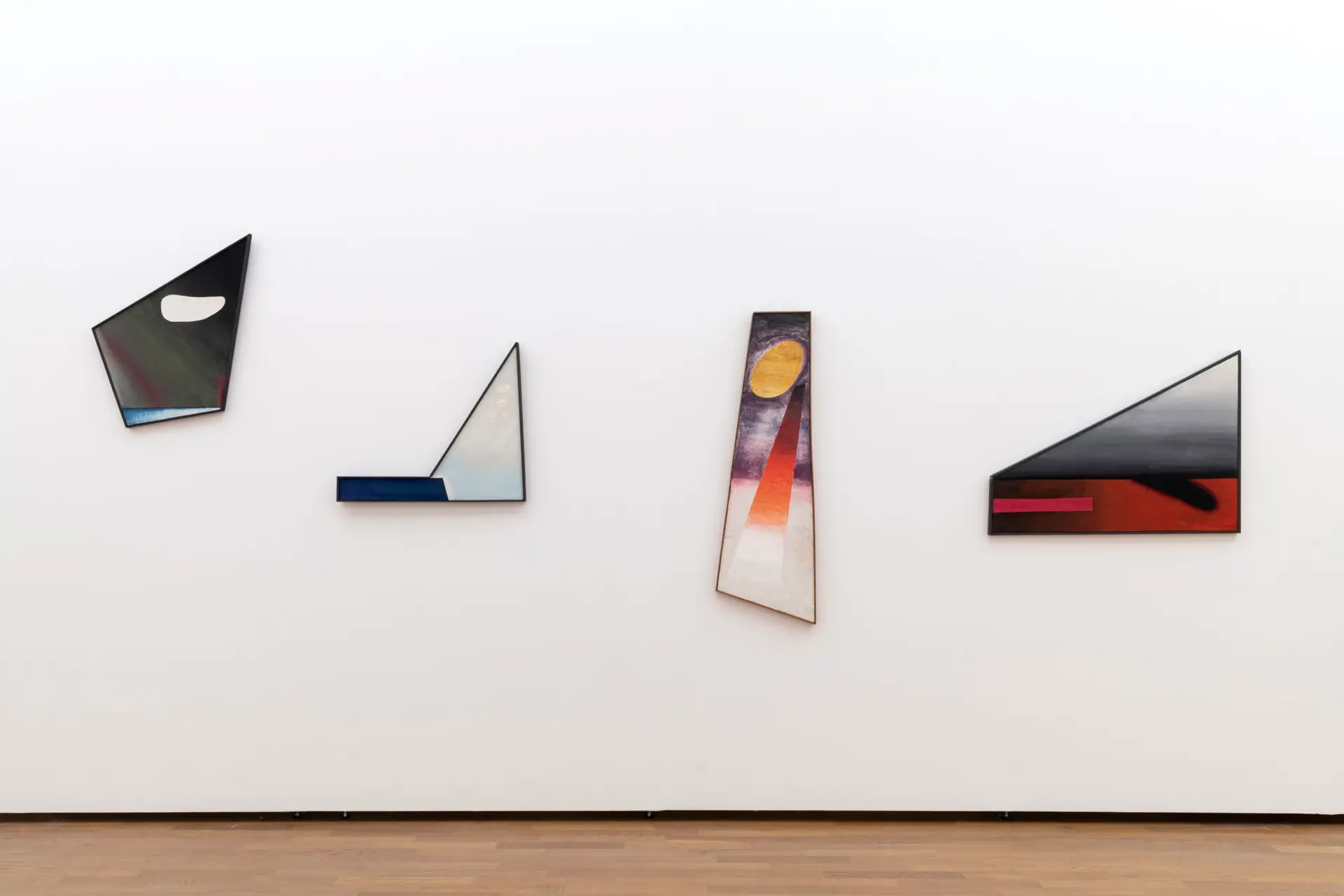 Blick in die Ausstellung "Rupprecht Geiger. Farbe, Licht, Energie". Fotografie zeigt frontal eine Wand mit vier Kunstwerken, die irreguläre Formate haben. Die Kunstwerke zeigen abstrakte Farben und Formen.