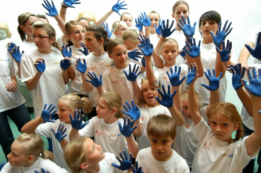 Kinder in weißen T-Shirts heben ihre Hände in die Luft, die blau angemalt sind.